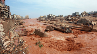 Water rushes down a street in Derna, eastern Libya. Destroyed buildings and houses are pictured on its banks.