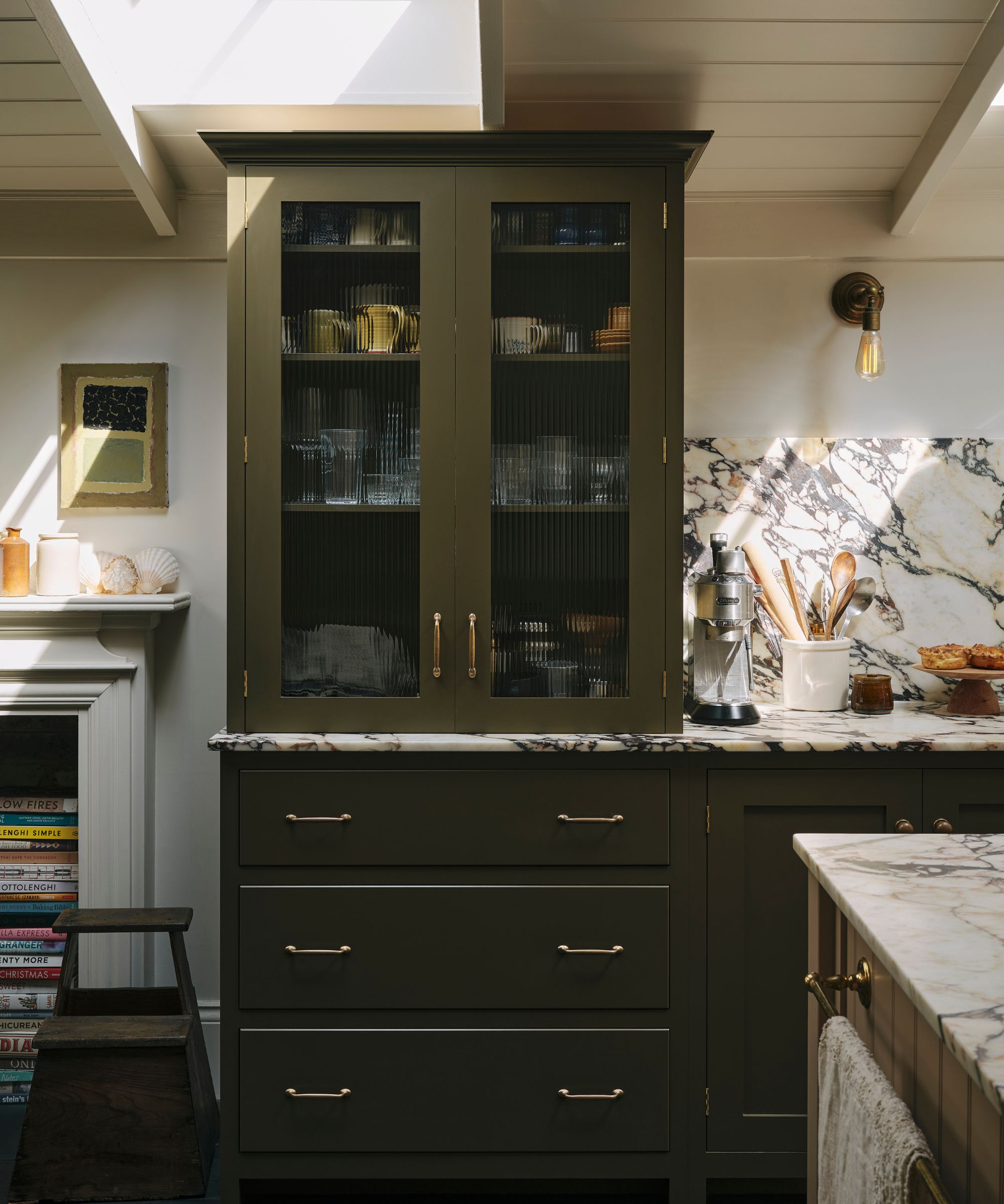 An olive green kitchen with marble countertops, warm white walls, and glazed cabinets