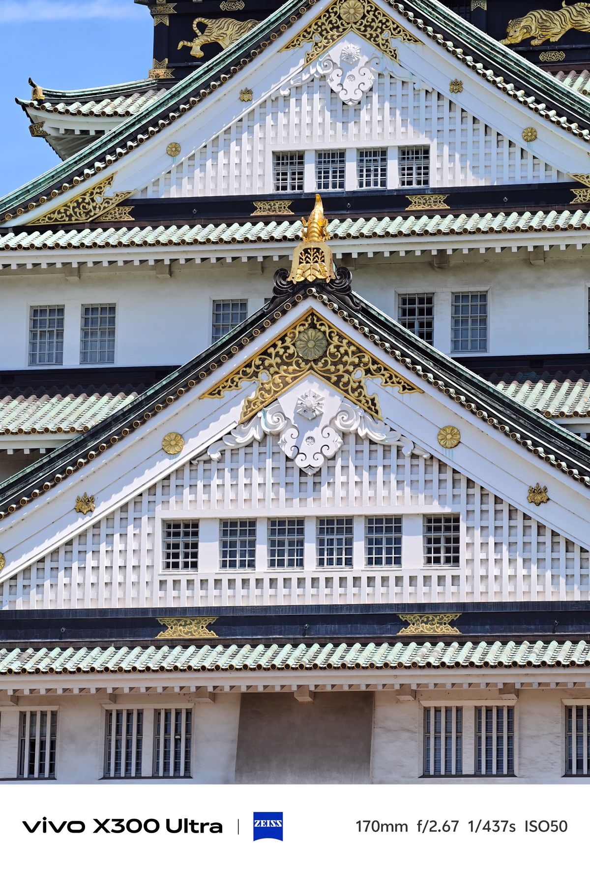 Architectural close-up of a white castle gable decorated with intricate gold leaf and green tiles.