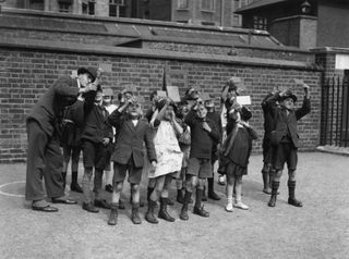 A schoolteacher and a group of children look up at the sky through photographic film.