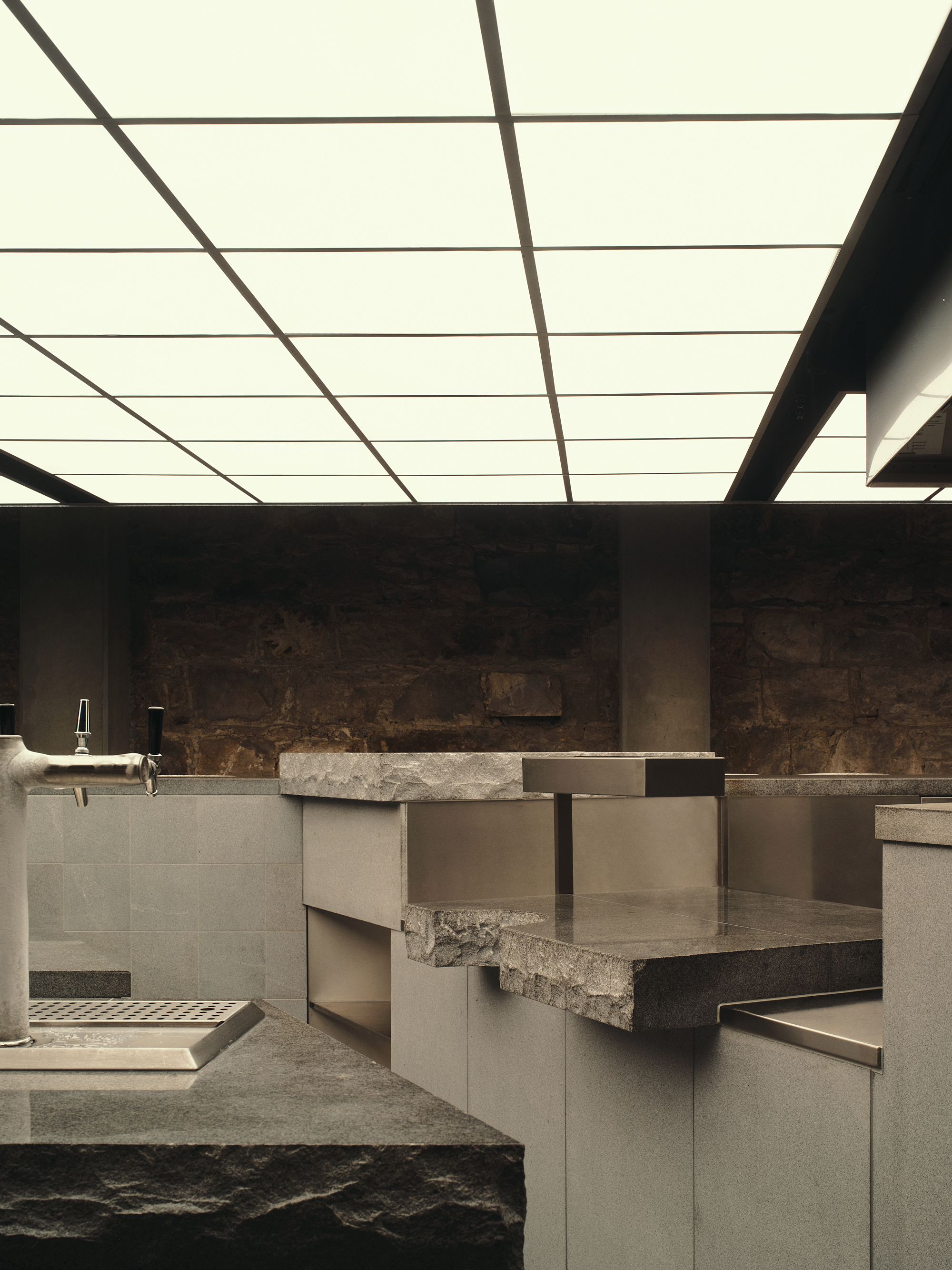 a bar tap sitting on top of a counter made from stone, alongside other stone counter tops underneath a ceiling completely lit up