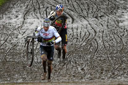 Mathieu van der Poel and Wout van Aert running through mud in a cyclo-cross race, shouldering their bikes