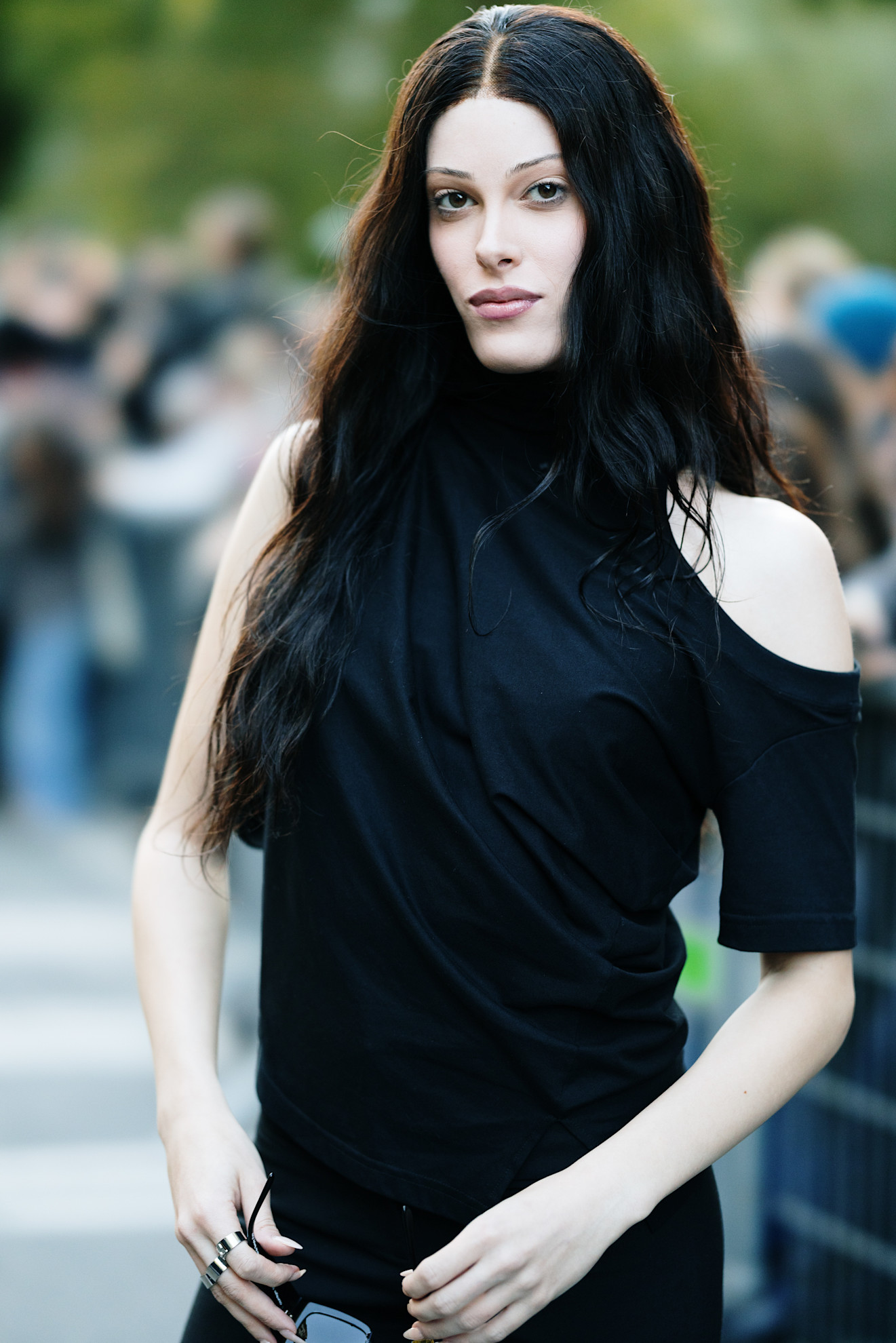 a pale woman with black hair and thin eyebrows wearing a black short sleeve top