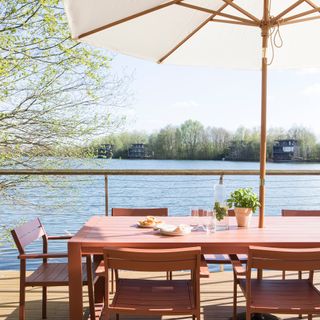 Rust-coloured outdoor table and chairs with cream parasol on terrace overlooking lake