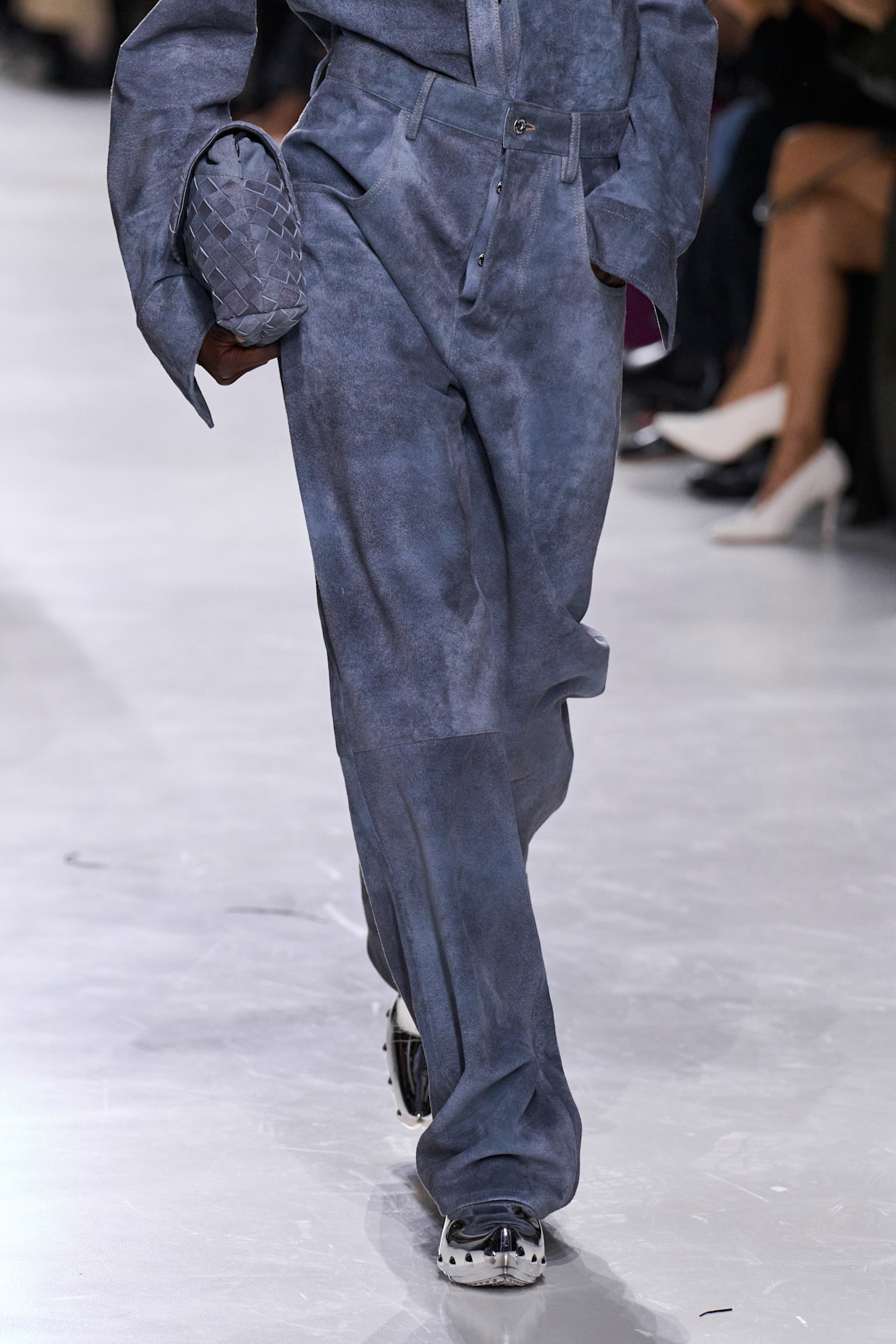 A Bottega Veneta model at the S/S 26 show wearing a suede blue outfit with silver clogs.