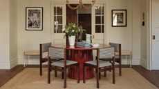 Image of a white dining room with a round, glossy red dining table with five black and white gingham dining chairs around it. There is a jute rug underneath the table.