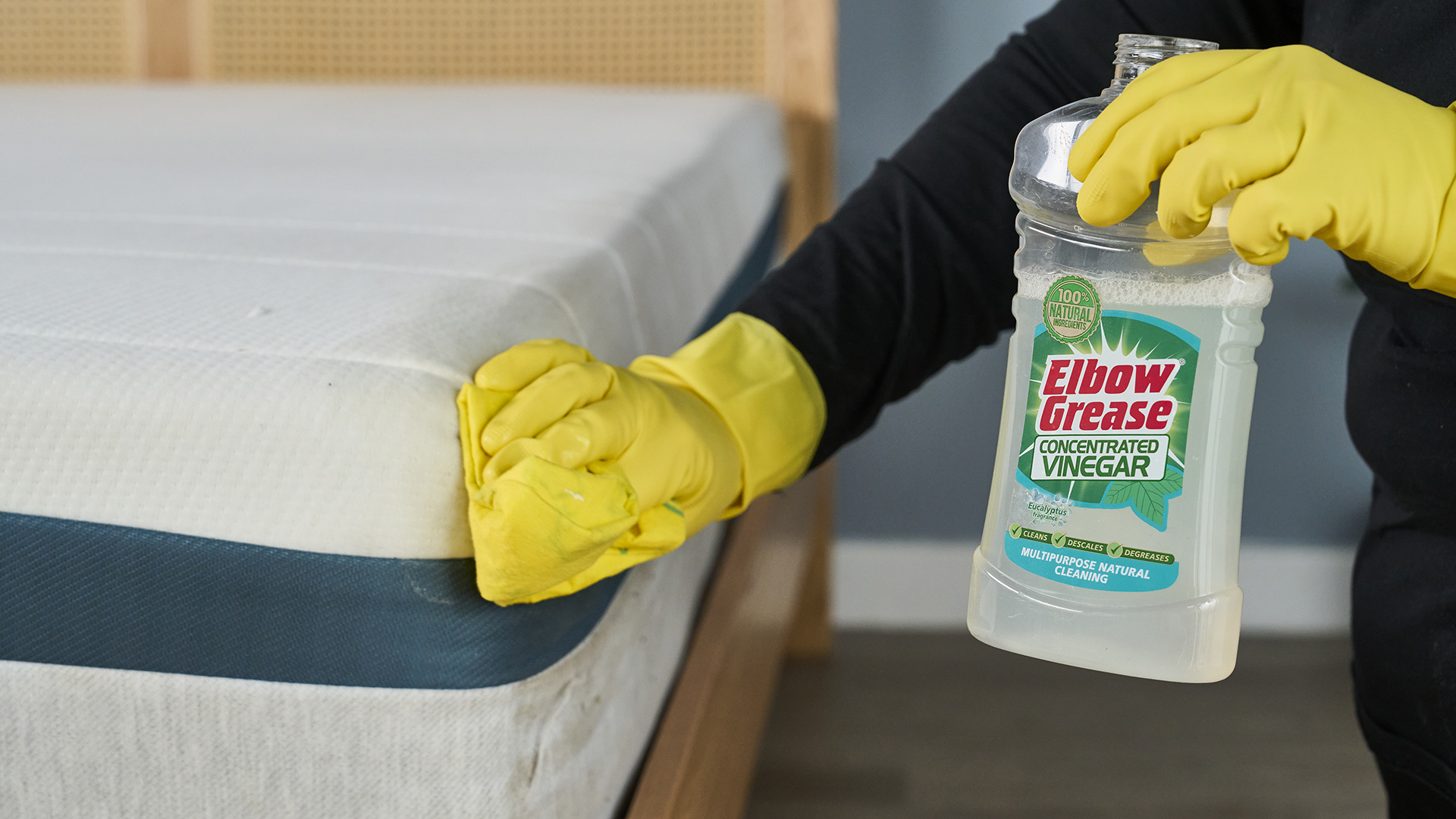 A woman using a cloth to clean a mattress while holding a bottle of vinegar