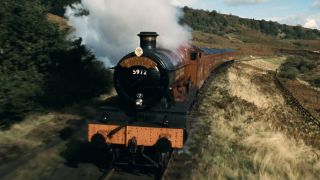 The Hogwarts Express on the move with steam coming out of it.