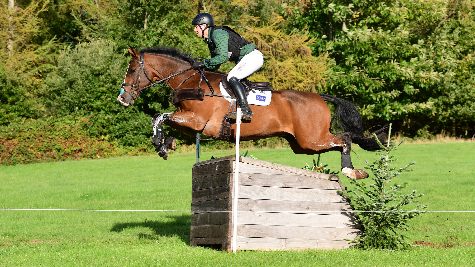 Max Warburton, a rider in a green top, rides Norway Van De Haar, a bay horse, over a narrow wooden cross-country fence at Bicton in October 2026