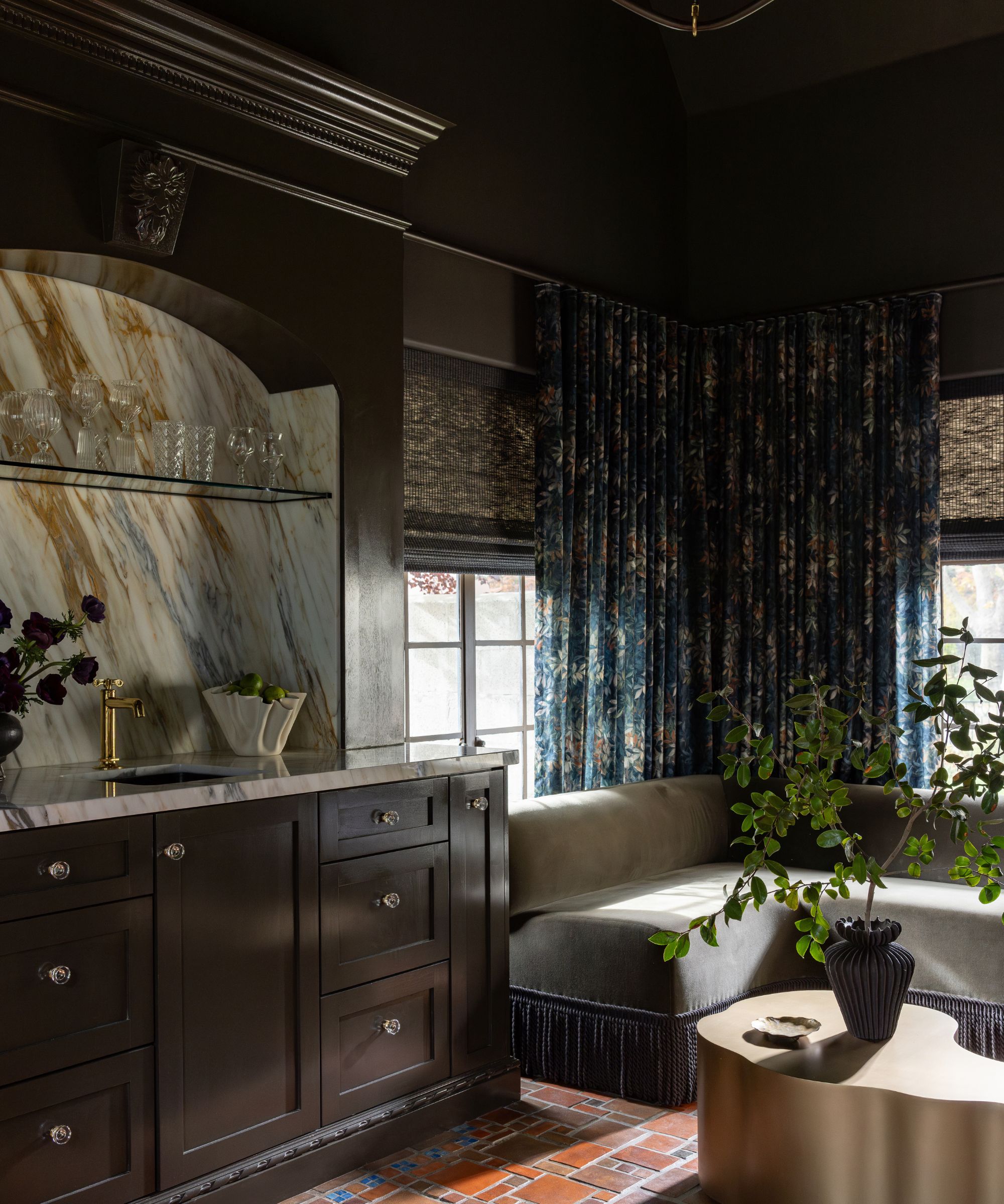 A home bar with warm black cabinets, marble counters, and a seating bench in the corner.