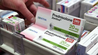 a man holds up a box of prednisone from a stack