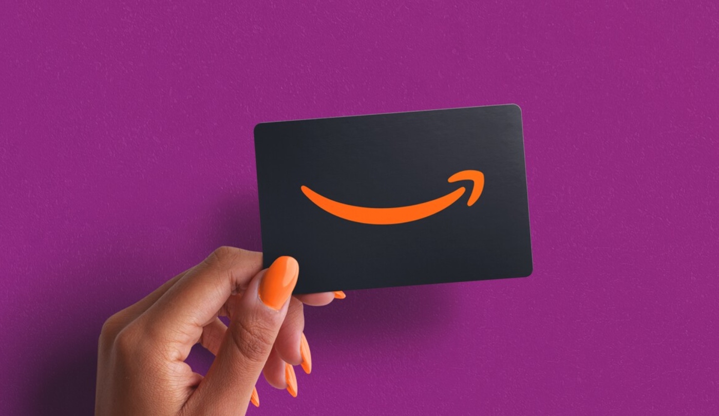 Purple background with person holding black Amazon gift card with orange Amazon logo on it