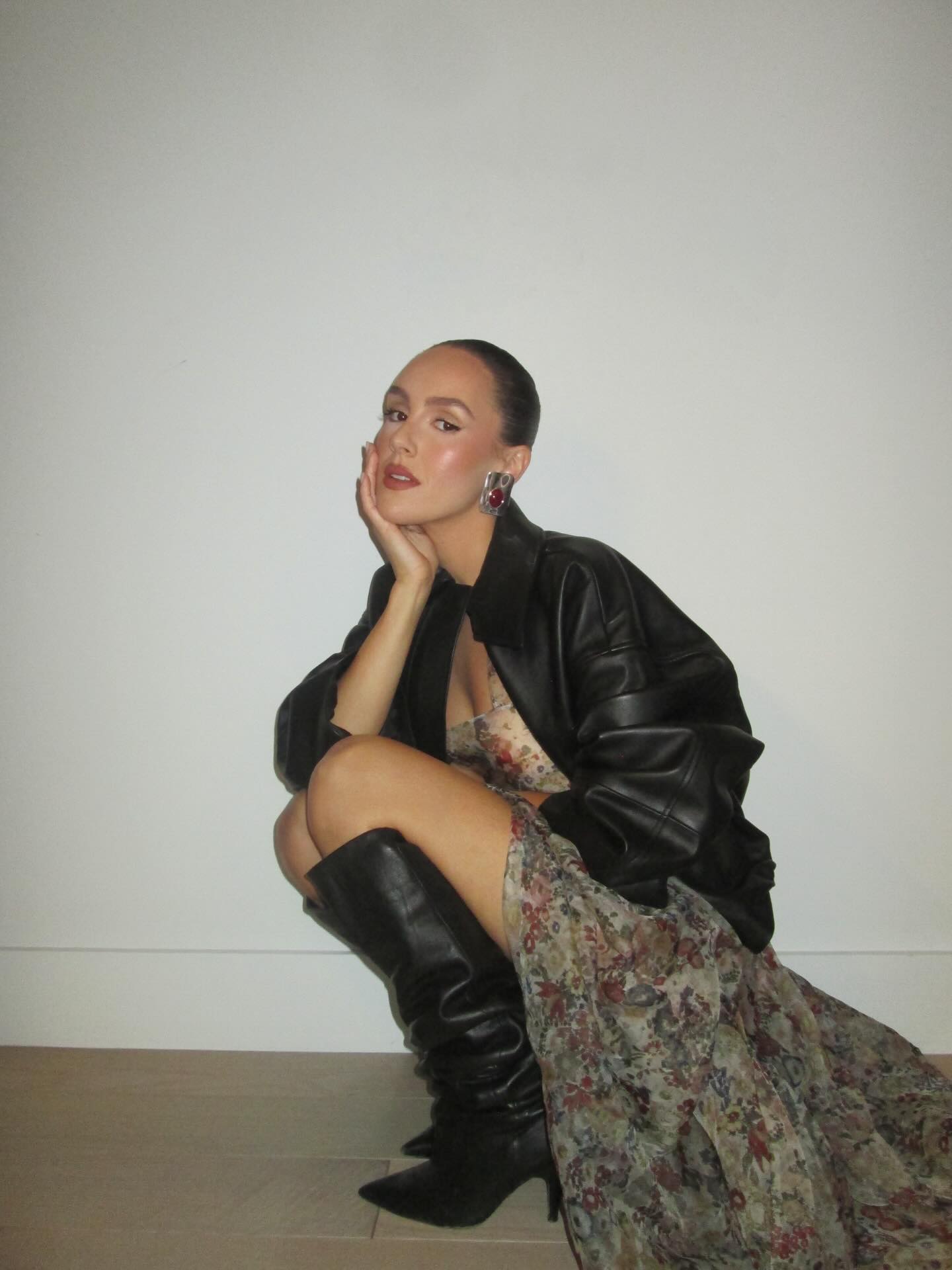 An image of @emmaleger wearing a floral dress from Khaite with a leather jacket and boots.