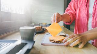 Woman putting slices of cheese on bread in kitchen