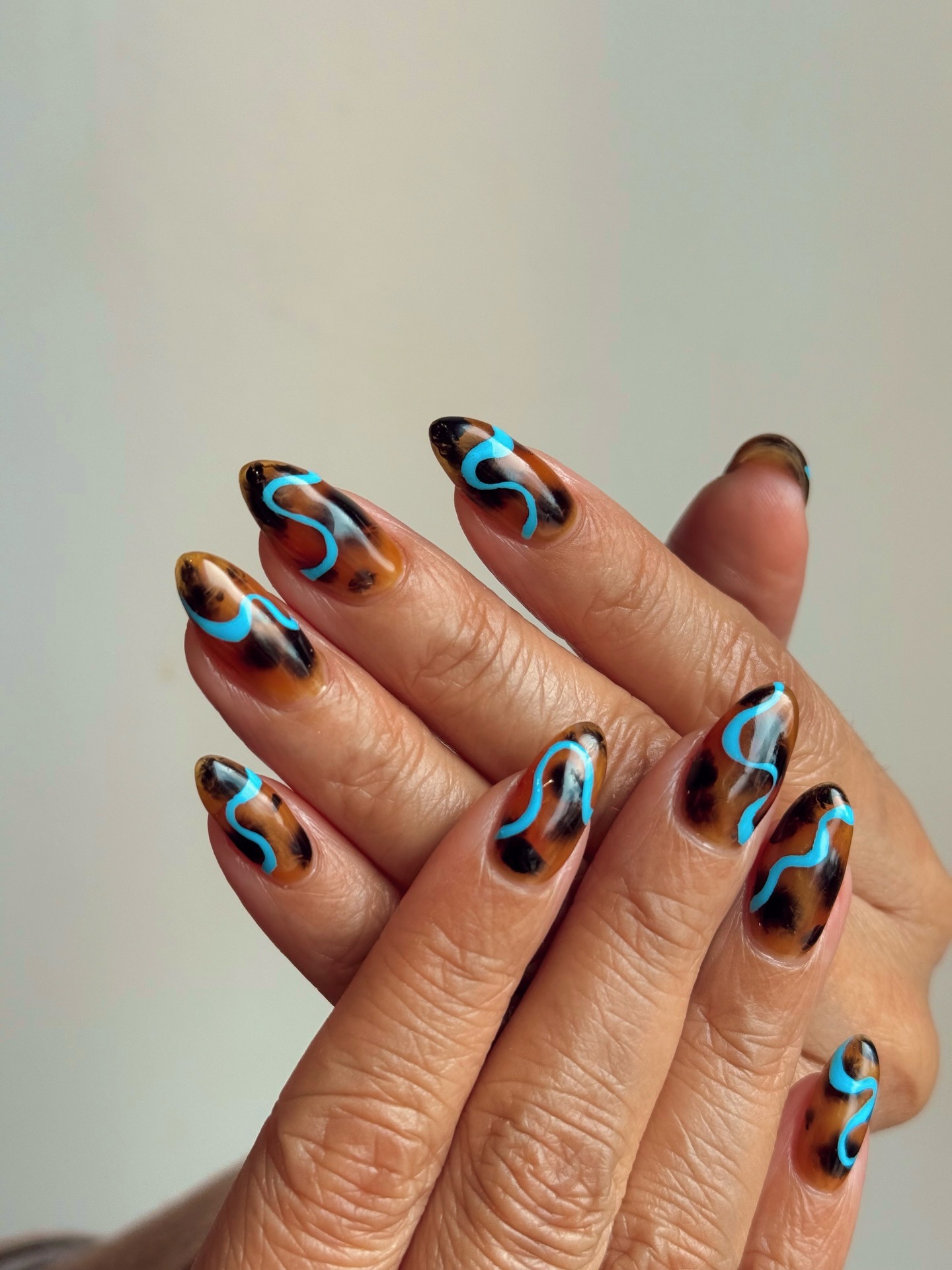 A tortoiseshell nail design with blue swirls