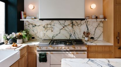 modern kitchen with timber cabinetry, marble countertops, white freestanding oven, floating marble shelves, a butlers sink, potted herbs, wall sconces, and a marble kitchen island