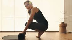 Woman doing heel touches exercise, rolling out yoga mat in studio