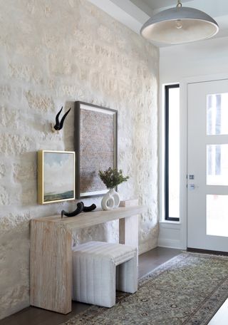 entryway with stone wall, wooden console table with hung art