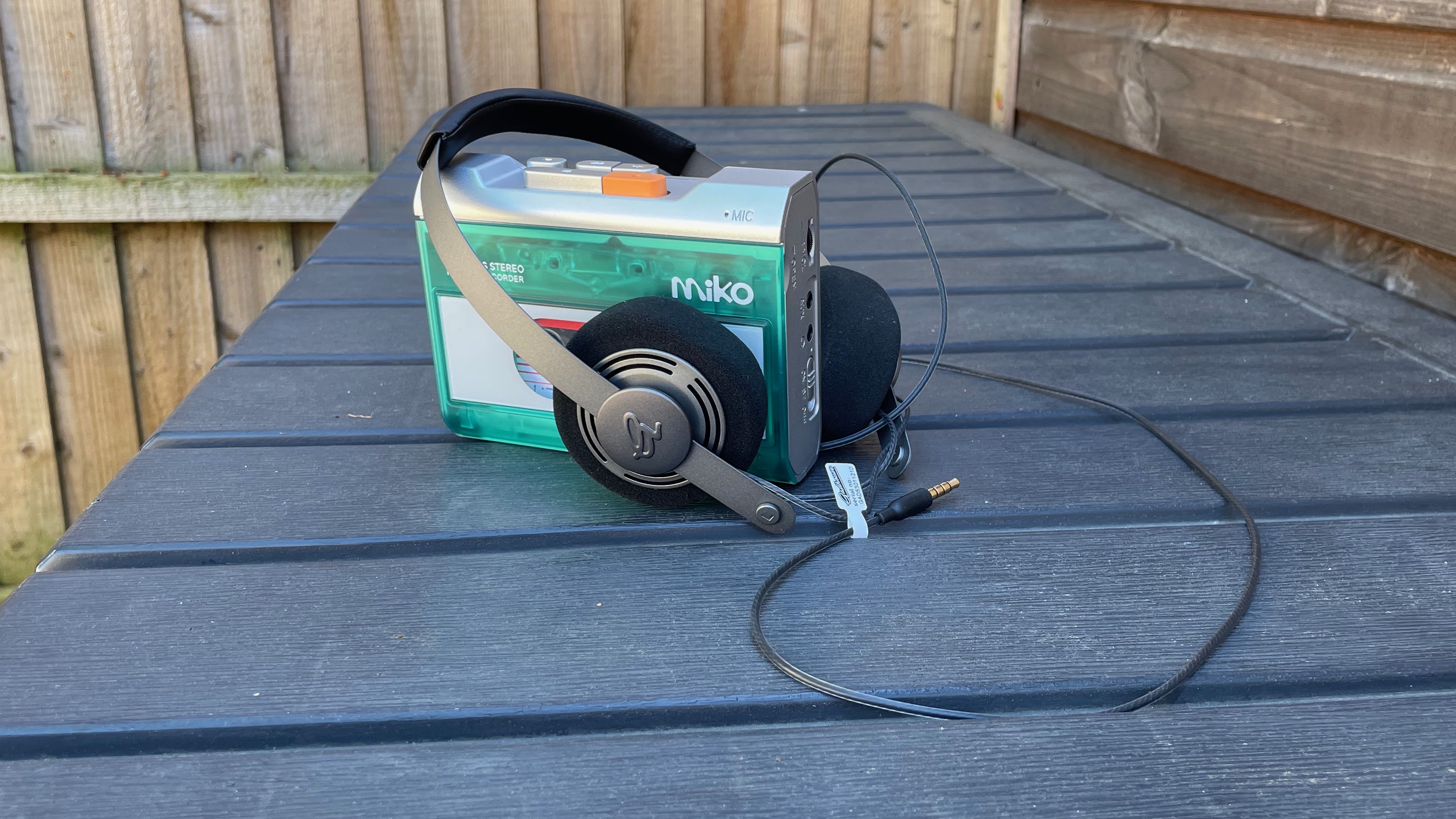 The Gadhouse Miko cassette player with the Gadhouse Wesley on-ear headphones on a black grooved surface in front of a garden fence.