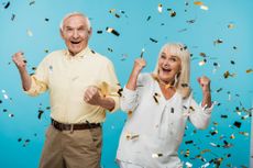 happy retired husband and wife gesturing near falling confetti on blue