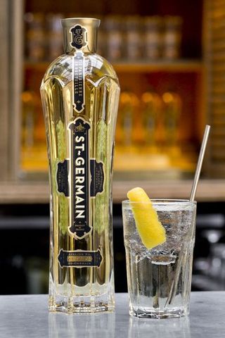 A bottle of St. Germain on a bar counter next to a cocktail.