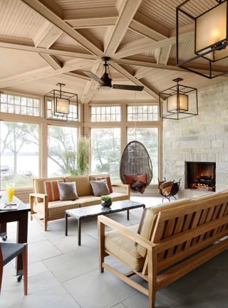 screened porch with wooden ceiling and exposed stone wall, wooden sofas, hanging chair and lanterns