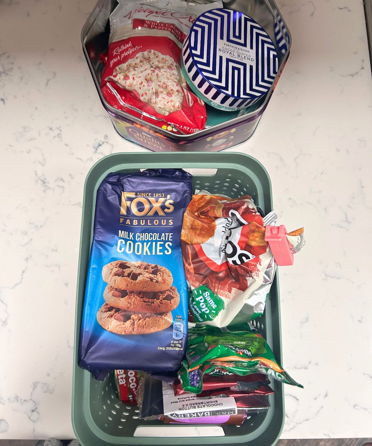 Snacks lining a green box and Quality Street tin
