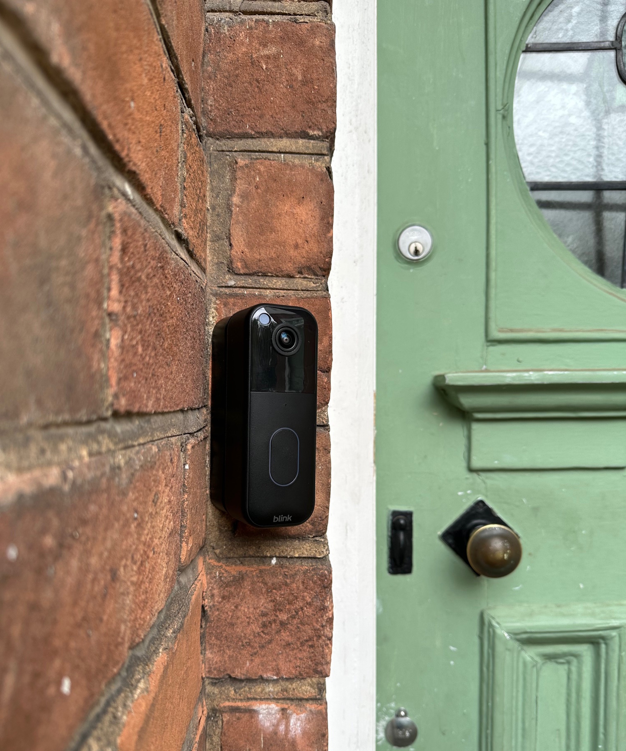 Black Blink video doorbell attached to outside wall next to green door