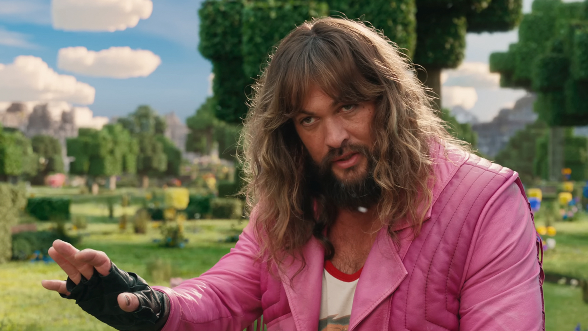 Jason Momoa in a pink jacket, with long hair and a beard in A Minecraft Movie
