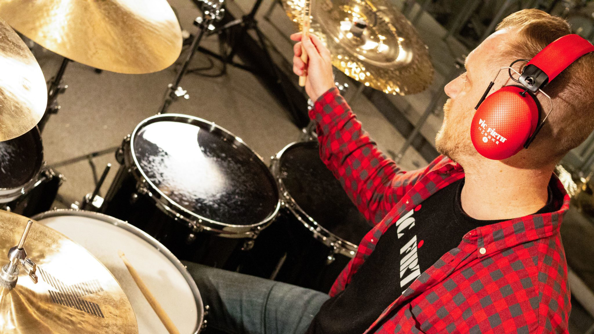 Man wearing a red pair of Vic Firth isolation headphones sat behind an acoustic drum kit