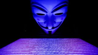 Anonymous mask overlooking a bright keyboard in a pitch-black room
