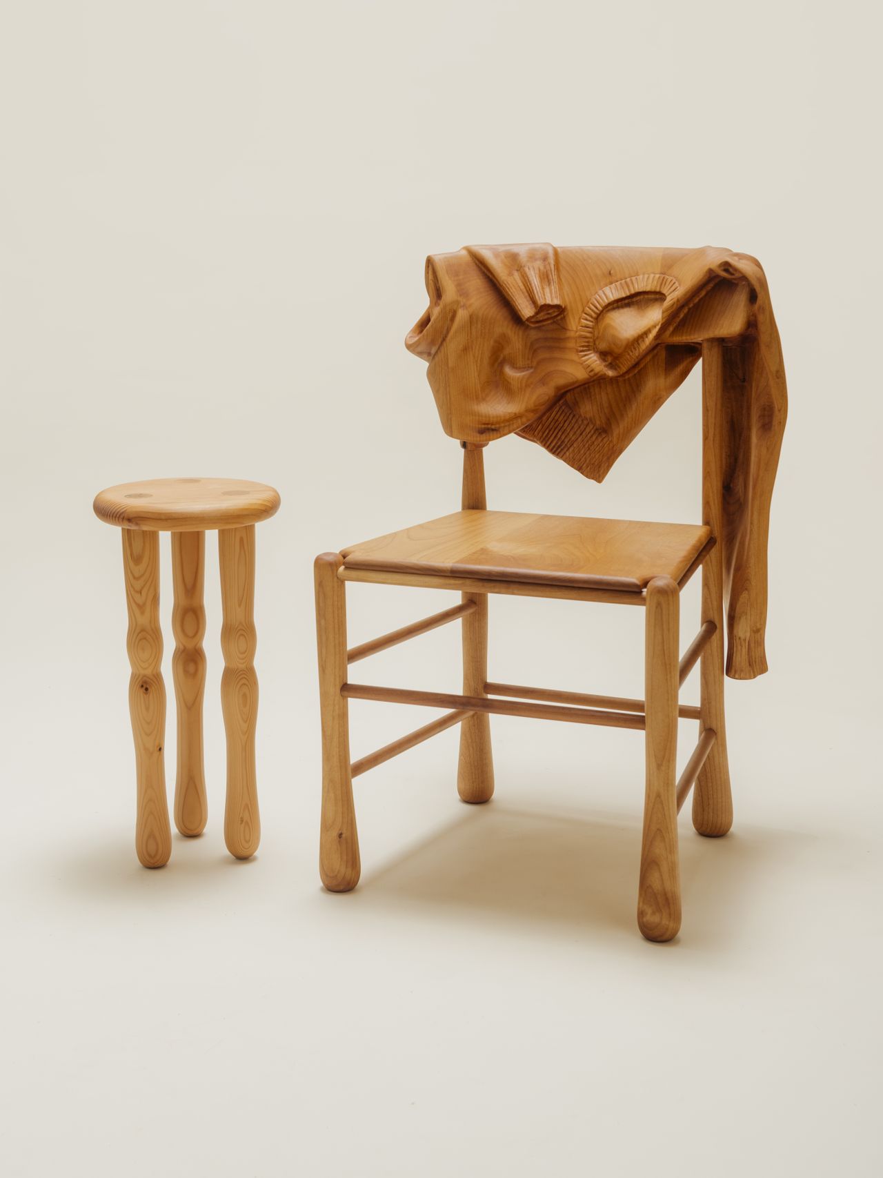 Wooden furniture items including a bed-site table, a chair, and a stool have surreally realistic textures mimicking the look of a T-shirt and a ribbon.