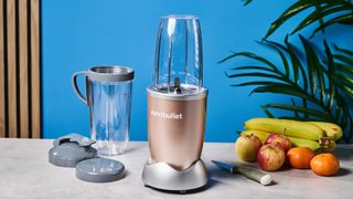 a champagne nutribullet pro 900w with fruit in the shot and a blue background