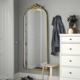 Bold ornate mirror on the wall beside a chest of drawers