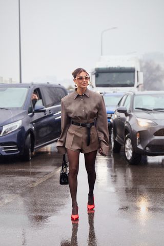 Guest wearing a brown blazer and matching short shorts with tights and red satin heels in Milan.