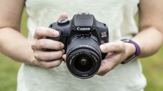En person som holder et systemkamera av typen Canon EOS 4000D i hendene.