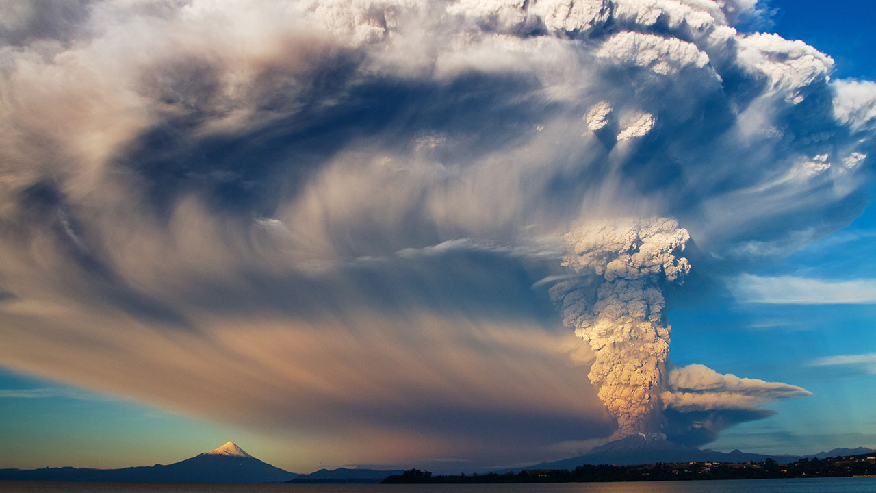 Calbuco volcano erupting with ash spreading across the blue sky