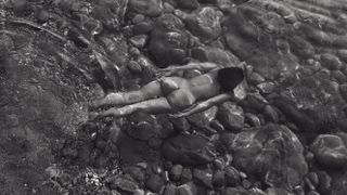 Black & white image of a naked woman floating face down in water