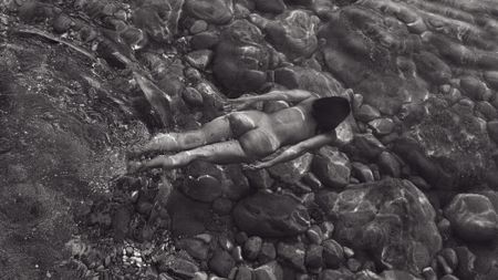 Black & white image of a naked woman floating face down in water