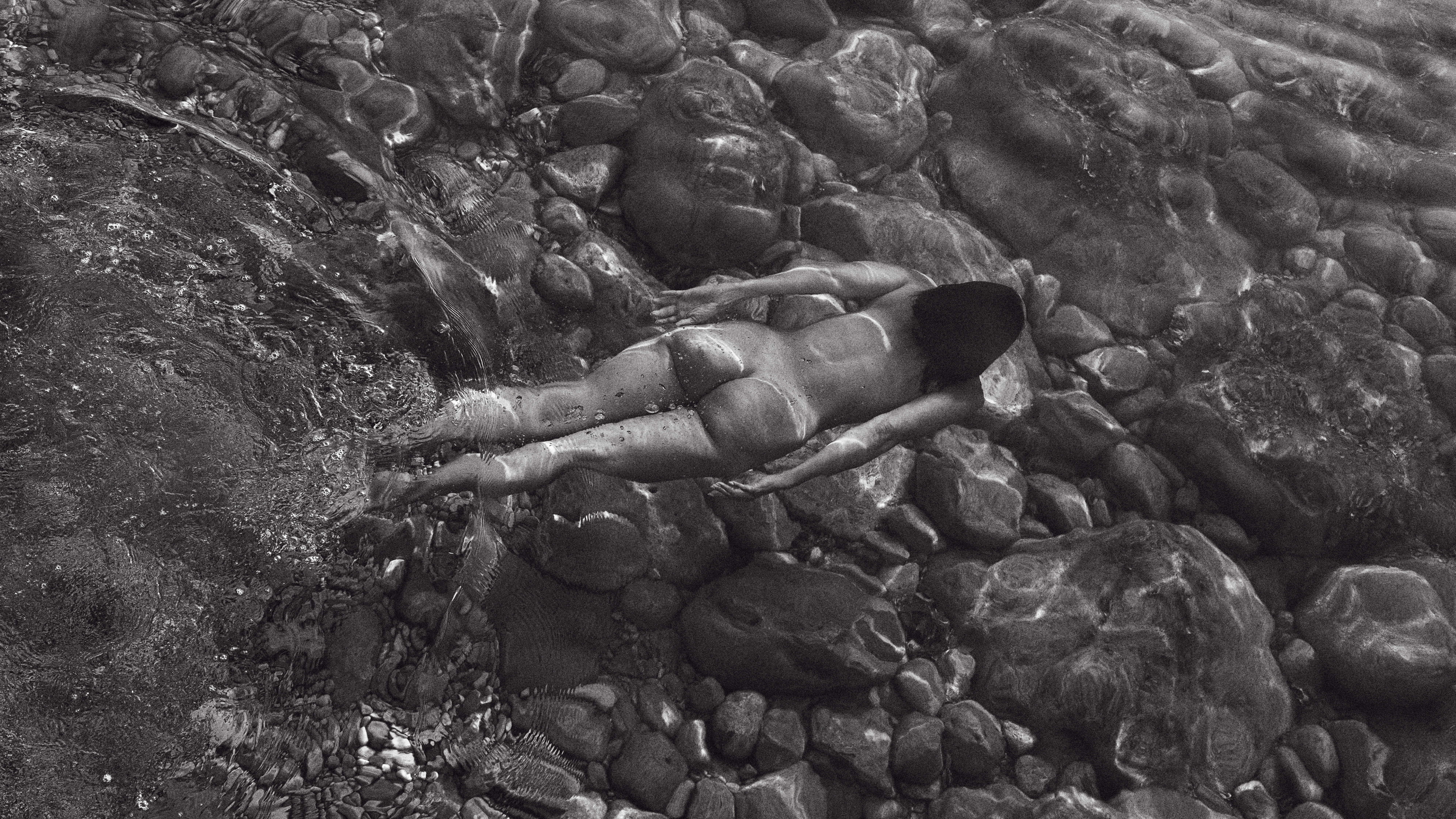 Black &amp; white image of a naked woman floating face down in water