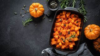 Roasted pumpkin pieces on a baking sheet with two small pumpkins nearby