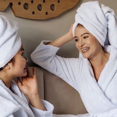 Two women in spa robes and towels chatting on beige sofa