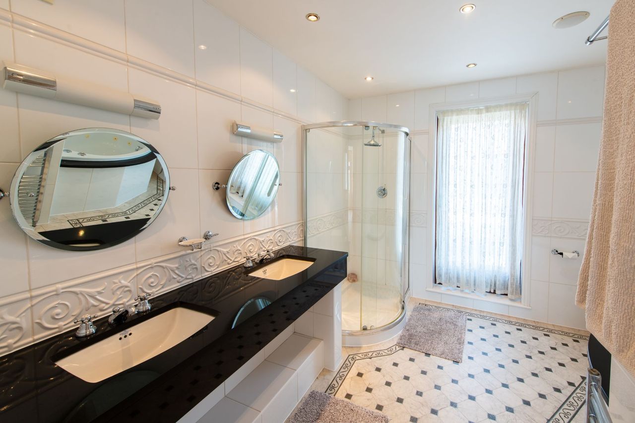 The bathroom has black sink tops and shower with curtain and black and white tiling for the floors and walls