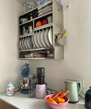 A white kitchen with a wall shelf with plates and colorful kitchen appliances