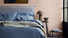 a bed with a gingham headboard and denim blue colored sheets with a rattan lamp