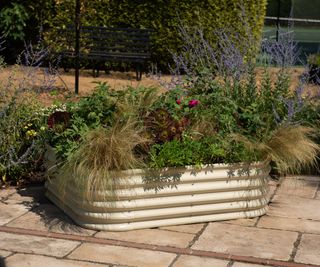 A corrugated metal raised bed filled with prairie style plants on a stone paved patio
