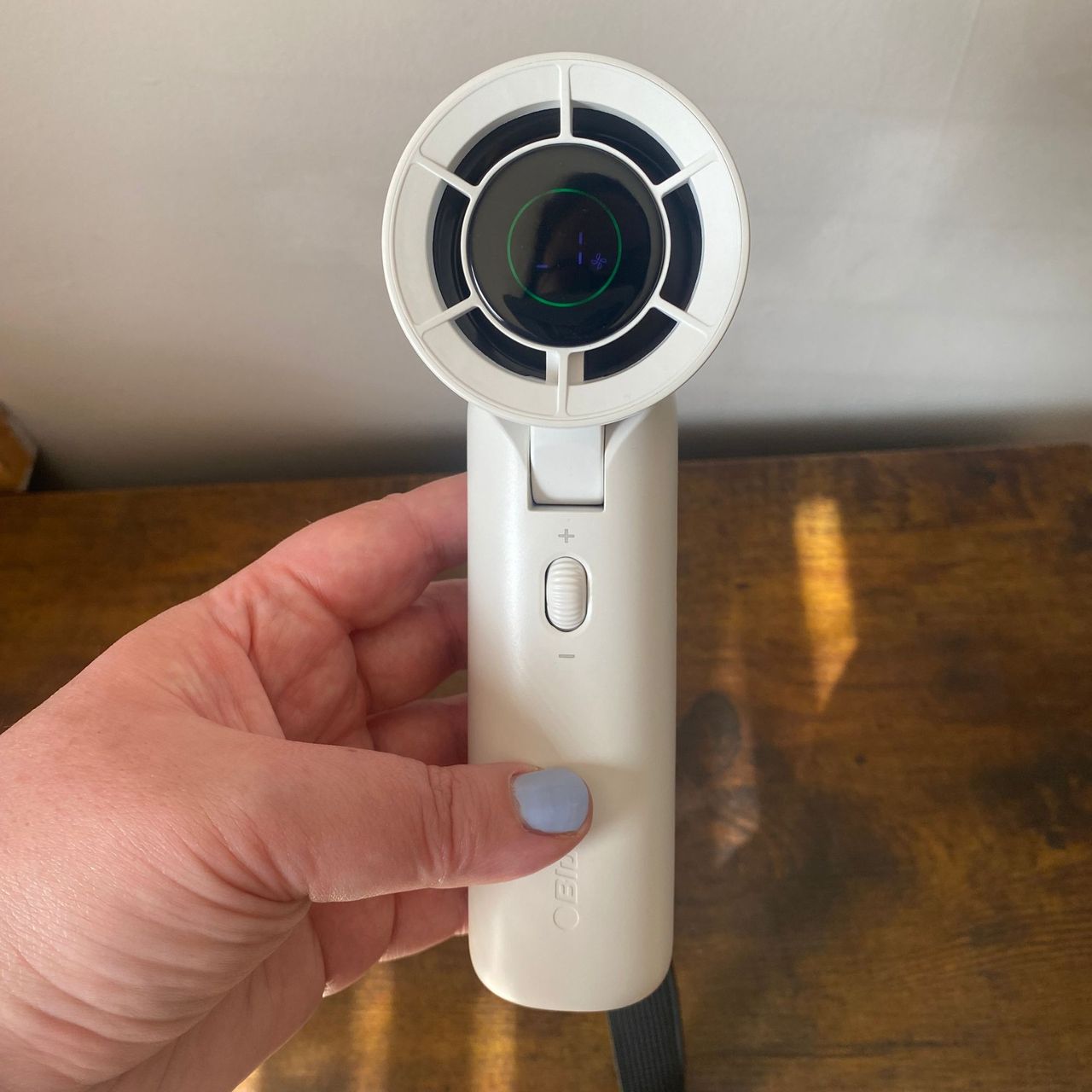Holding the Blueair AlwaysCool Portable Handheld Fan over a wood-look sideboard