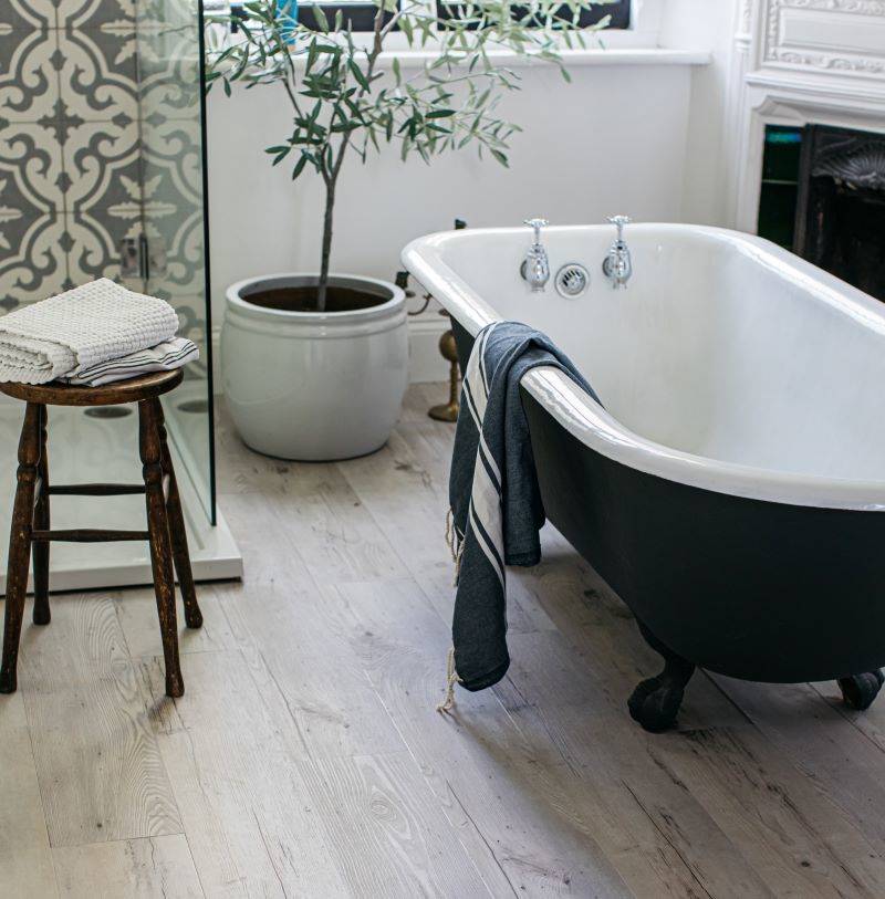 A bathroom idea with a black freestanding bath and wooden stool with wooden effect LVT flooring