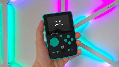 Green and Black Taito Super Pocket handheld with RGB lights in backdrop and sad text face on screen