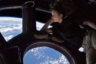 an astronaut leaning against a set of circular windows with earth below and space in behind